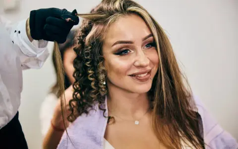 Fryzjerka tworzy loki na włosach kobiety z wyraźnymi, chunky highlights.