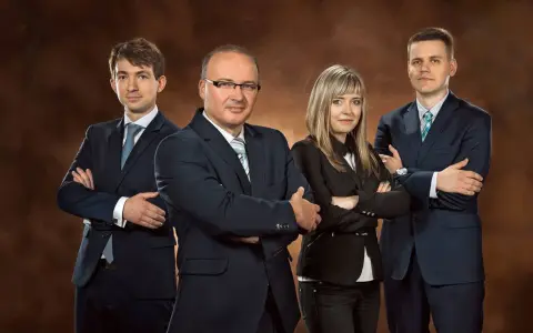 Cztery osoby w garniturach stojące z rękami skrzyżowanymi na piersi.