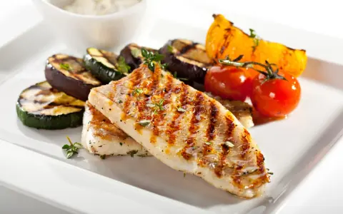 Gebratener Seelachs mit gegrilltem Gemüse wie Zucchini, Aubergine und Tomaten, garniert mit Kräutern.