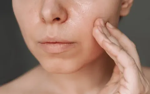 Une main touche délicatement la joue d'une femme, révélant une peau lumineuse, idéale pour une routine peau grasse.