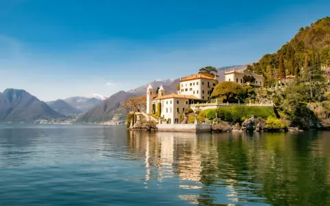 A scenic journey from Milan to Lake Como reveals this stunning villa on the water's edge, with mountains in the distance.