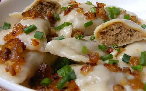 Pyszne pierogi z mięsem, okraszone skwarkami i szczypiorkiem, kuszą swoim domowym wyglądem.