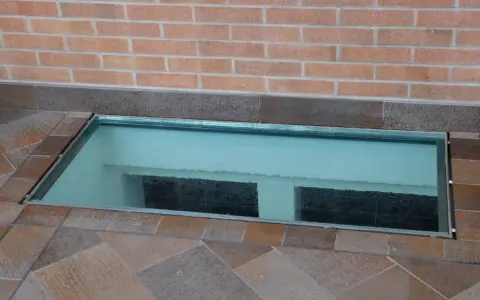 Bocche di lupo moderne in vetro, incastonate in un pavimento di piastrelle color terra, illuminano uno spazio sottostante.