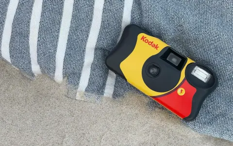 Aparat jednorazowy firmy Kodak leży na plaży obok ręcznika. Idealny do uchwycenia letnich wspomnień.