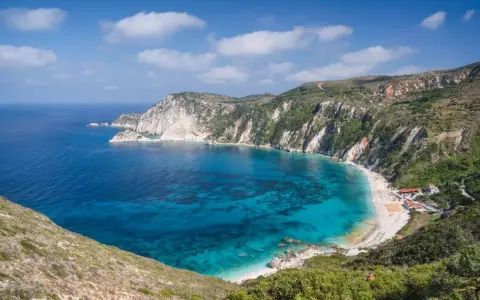 Malownicza zatoka z turkusową wodą i piaszczystą plażą, otoczona stromymi, zielonymi klifami. To idealne miejsce na wypoczynek na wyspie na Morzu Jońskim.