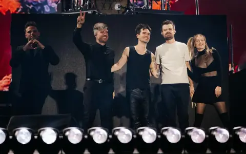 Medlemmar av Panic! at the Disco på scenen, en gör hjärta med händerna, en annan vinkar med två fingrar.