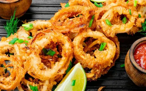 Aros de calamar rebozados y fritos, servidos con limón y salsa de tomate. Ideales para recetas con calamares.
