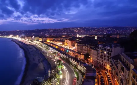 Night view of the Promenade des Anglais from Castle Hill, Nice, France, with city lights twinkling and car trails on the road.