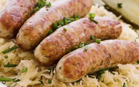 Aksamitna biała kiełbasa w kiszonej kapuście, posypana szczypiorkiem. Pyszne danie gotowe do podania.