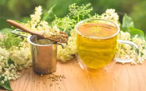 Aromaticzny napar z czarnego bzu, suszone kwiaty na łyżce i metalowe sitko.