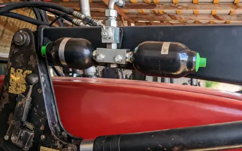 Dwa akumulatory hydrauliczne zamontowane na ładowaczu. Pomocne przy wyborze, jak dobrać akumulator hydrauliczny do maszyn rolniczych.