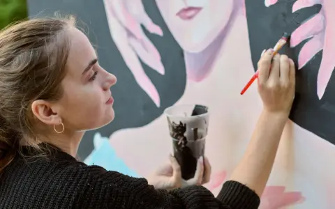 Une jeune artiste entrepreneur peint un portrait. Elle tient un pinceau et un gobelet de peinture noire.