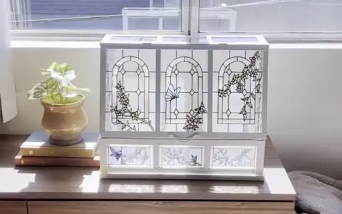 Boîte à bijoux ornée de vitraux décoratifs représentant des papillons et des fleurs, posée sur une commode en bois.