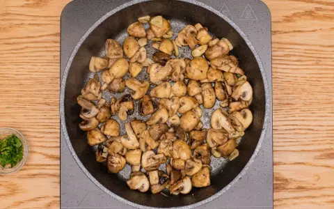 Champiñones al ajillo dorándose en sartén, con ajo y perejil picado al lado.