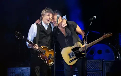 Bruce Springsteen und Paul McCartney umarmen sich auf der Bühne, beide mit Gitarren.