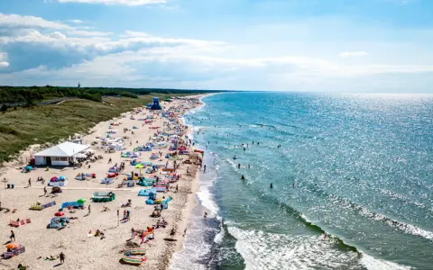 Słoneczna plaża w Darłówku pełna ludzi, kolorowych parawanów i namiotów. Woda w Bałtyku błyszczy, a fale zachęcają do kąpieli. To idealne miejsce na wakacyjne atrakcje.