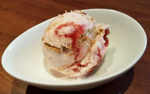 Ein Löffel cremiges strawberry cheesecake eis mit Erdbeersauce und Keksstückchen in einer weißen Schale.