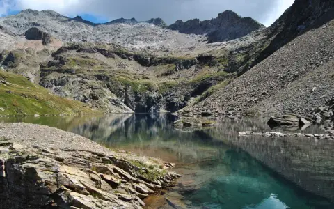 Riflessi perfetti sul lago nero, incastonato tra montagne rocciose e verdi pendii.