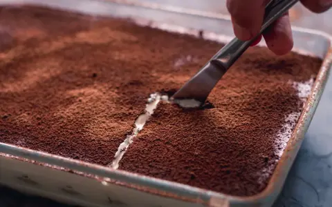 Kto pyta, czy mascarpone jest fit, gdy widzi tak kuszące tiramisu? Nóż kroi deser, odsłaniając kremową warstwę.