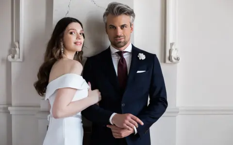 Elegancki pan młody ślub cywilny w granatowym garniturze i jego uśmiechnięta narzeczona w białej sukni.
