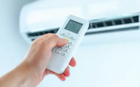 Dłoń trzymająca pilot do klimatyzatora, ustawiająca temperaturę. Ogrzewanie klimatyzatorem to komfort.