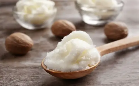 Ein Holzlöffel voller cremiger shea butter haare, daneben Nüsse und Schalen mit der Butter.