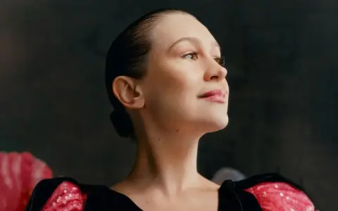 Joanna Newsom, con su cabello recogido y un vestido negro con detalles brillantes, mira hacia arriba con una expresión serena.
