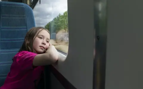 Dziewczynka wpatrzona w okno pociągu, zastanawia się, od ilu lat można jeździć samemu pociągiem.
