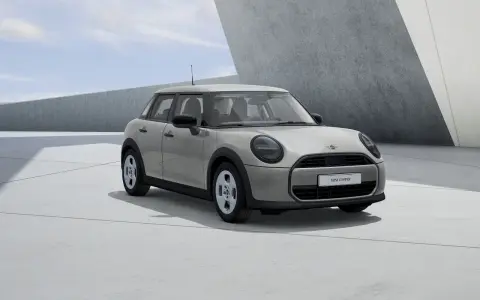 Mini Cooper 5 puertas en color gris claro, con llantas plateadas, estacionado en una zona de concreto con arquitectura moderna.