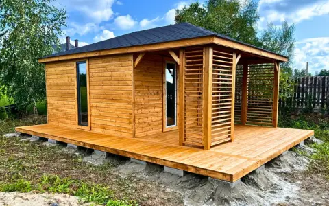 Drewniany domek narzędziowy z werandą, posadowiony na solidnym podłożu z bloczków betonowych.