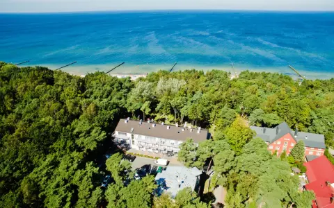 Widok z lotu ptaka na hotel otoczony lasem, z widokiem na morze. Idealne miejsce na wakacje, sprawdź nasz tui kod rabatowy!