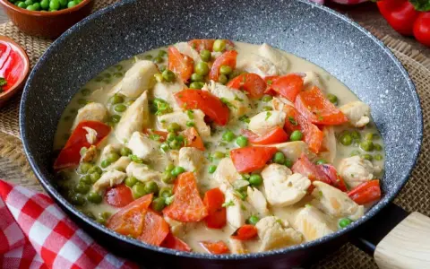 Hähnchen-Curry mit Erbsen und Paprika in cremiger Sauce – ein leckeres und gesundes Mittagessen, serviert in einer Pfanne.
