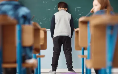 Chłopiec stoi przed tablicą z zadaniami matematycznymi.