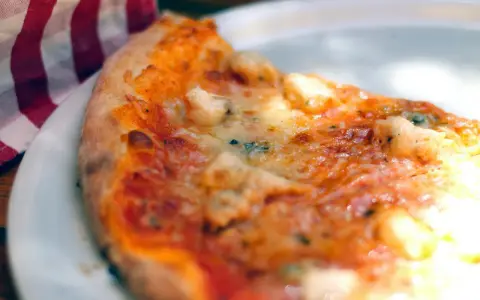 Tranche de pizza appétissante sur une assiette blanche, avec une serviette à carreaux rouges et blancs. Une recette parfaite avec de la farine sans gluten pour pizza.