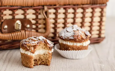 Zwei leckere bienenstich muffins mit Mandel-Topping und cremiger Füllung stehen vor einem Picknickkorb.