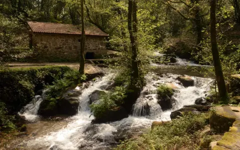 Antigua casa de piedra junto a un río con cascadas, ideal para una ruta senderismo Vigo.