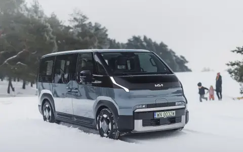 Szary elektryczny minivan Kia EV9 na śniegu, z rodziną w tle.