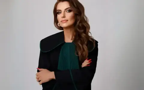 Kobieta w todze prawniczej, z rękami skrzyżowanymi na piersi, na jasnym tle.