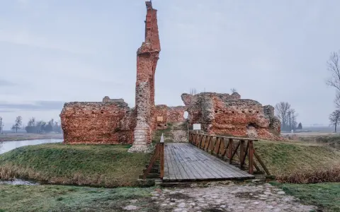 Ruiny zamku w okolicach Łodzi tak do 100 km. Drewniany mostek prowadzi do ceglanych murów.