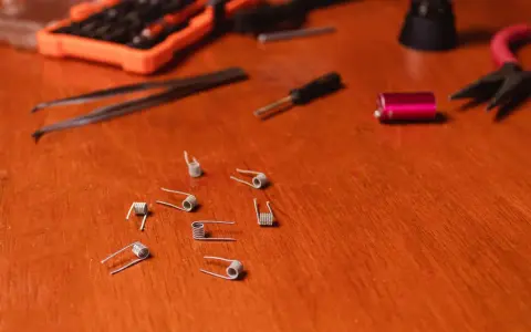 Varias resistencias comerciales de vapeo esparcidas sobre una mesa de madera, junto a herramientas como pinzas y un destornillador.