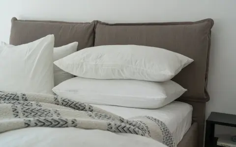 Lit douillet avec deux oreillers blancs empilés, une couverture à motifs et un drap housse ou protège matelas immaculé.