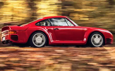 Czerwony Porsche 959 pędzi przez jesienny las, liście tworzą rozmyte smugi.