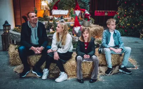 Familj njuter av en mysig stund vid en juldekoration med tomtar och gran. En härlig svensk julkänsla.