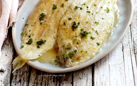 Sogliola alla mugnaia dorata e succulenta, cosparsa di prezzemolo fresco, servita su un piatto ovale.