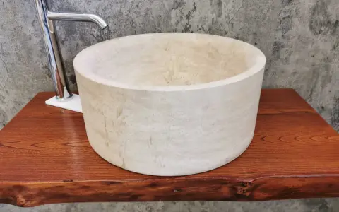 Lavabo cilindrico in pietra naturale chiara, con rubinetto cromato, su un piano in legno grezzo. Un esempio di come i nomi delle pietre naturali si trasformano in design unici.