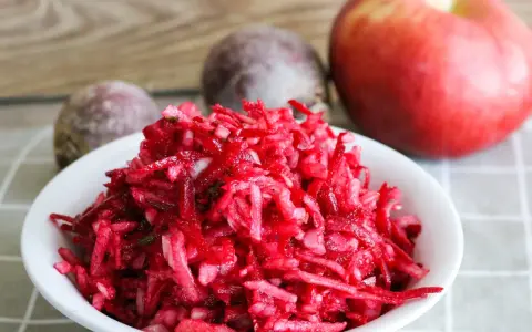 Frischer Salat aus rote Bete raspeln, mit einem Apfel und ganzen Rote Beten im Hintergrund.