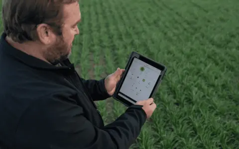 Farmer uses a tablet to monitor crop health and optimize yields, showcasing the power of digital farming in a lush green field.