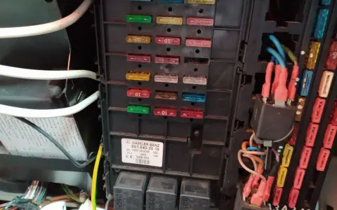 Panel bezpieczników w Mercedesie GL. Widoczne bezpieczniki i przekaźniki, a także etykieta z opisem.