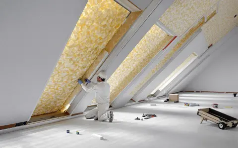 Un ouvrier installe un matériau isolant jaune texturé dans un grenier, assurant le meilleur isolant thermique pour la maison.
