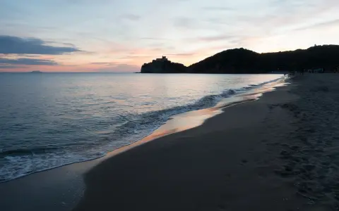 Tramonto sulla costa della Toscana, con un castello su una collina e il mare calmo. Un ricordo di vacanza con un neonato.